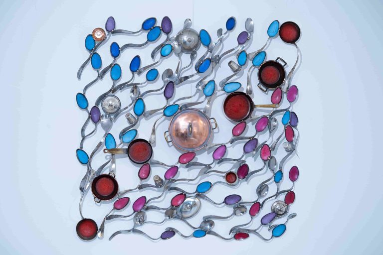 L’œuvre de l’artiste Kymia est une installation murale unique qui met en scène des ustensiles de cuisine réorganisés et mélangés. Du cuivre, de l’inox, de l’étain et des couverts tels que des fourchettes et des cuillères sont habilement assemblés pour créer une composition visuellement attrayante. Les éléments semblent avoir été transformés en une forme souple, et l’agencement des couleurs s’harmonise parfaitement avec la couleur de l’acier.