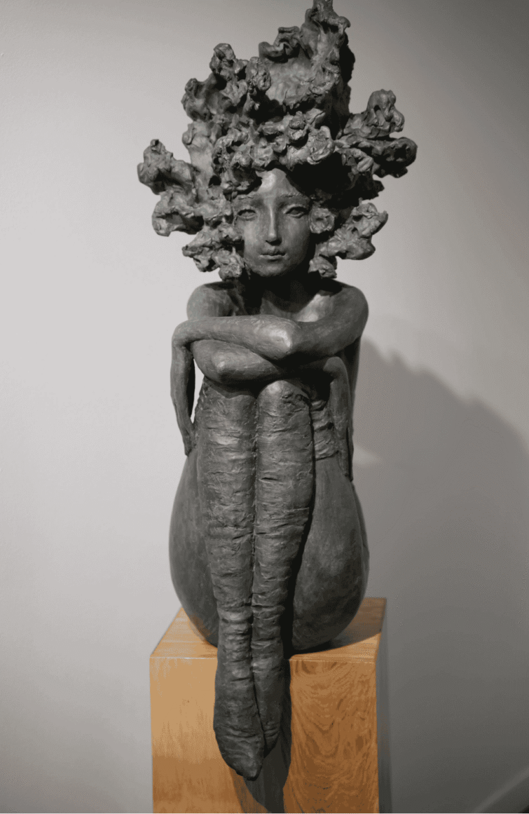 Sculpture en bronze représentant une femme debout, au corps allongé et aux bras croisés, surmontée d’une chevelure abondante évoquant un amas de formes végétales, présentée sur un socle en bois.